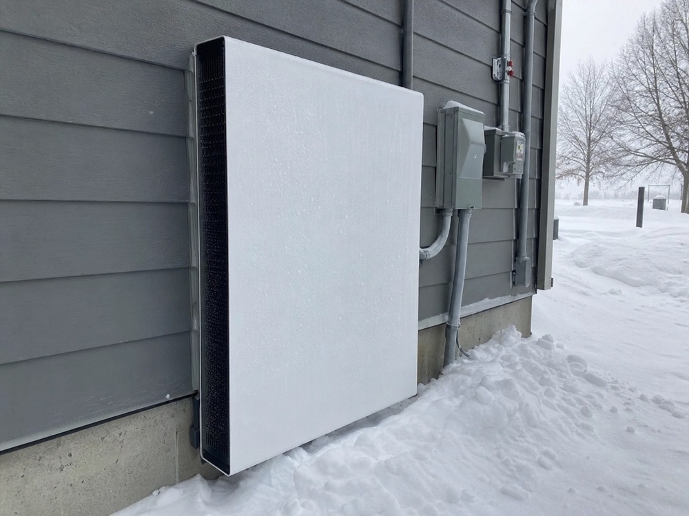 Tesla Powerwall mounted on a grey-sided home exterior in deep winter, surrounded by snow drifts — operating reliably in cold Ontario climate